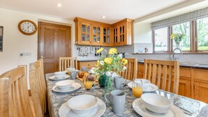 Un coin repas avec une table mise pour le petit-déjeuner, des meubles en bois, une horloge et une fenêtre donnant sur un beau paysage.