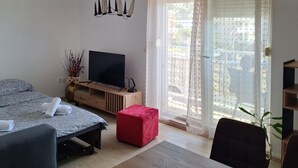 Une chambre moderne avec un lit, une télévision, un pouf rouge, une table en bois et une vue dégagée sur l’extérieur grâce à une grande fenêtre.