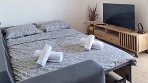 Une chambre moderne avec un lit, deux oreillers, une télévision, une table de chevet en bois et un vase contenant des fleurs séchées.
