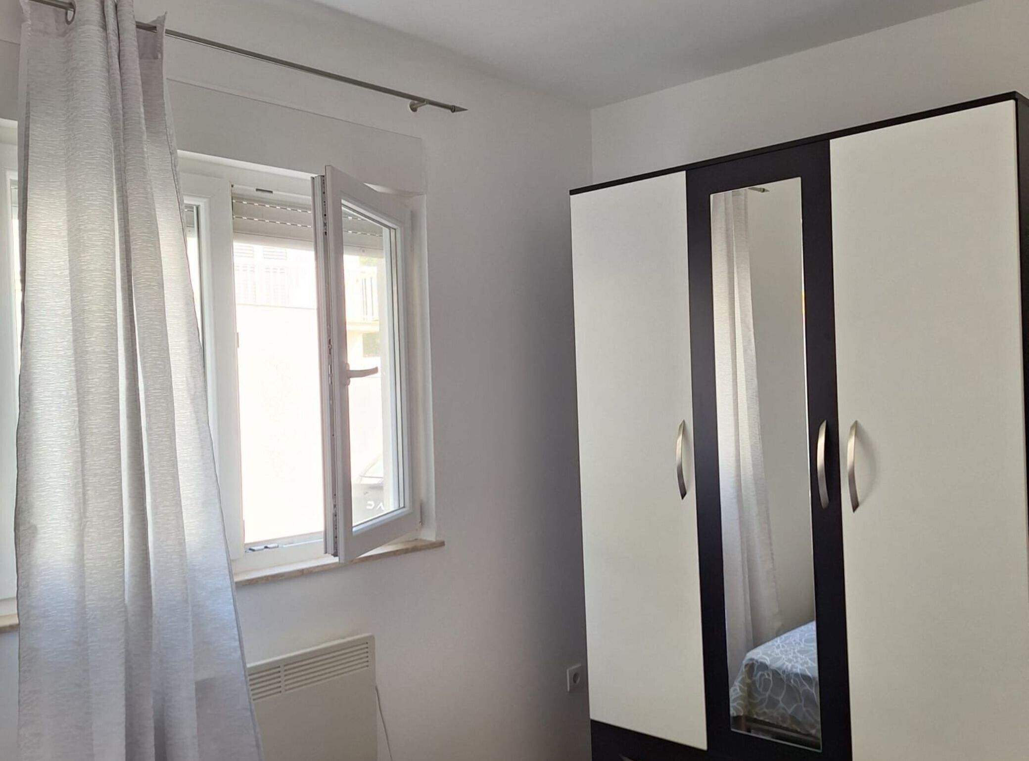 Une pièce avec une fenêtre, un radiateur et une armoire dotée d’un miroir.