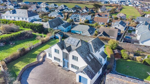 A coastal residential area with houses, a large white building with a blue door, and a view of the sea. - 5 Bed in Trevone (oc-s30762) (Trevone)