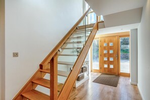 A modern staircase with wooden steps and glass railings leading to a door with frosted glass panels. - 5 Bed in Trevone (oc-s30762) (Trevone)