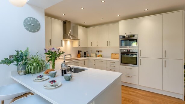 Eine moderne Küche mit weißen Schränken, einer zentralen Kochinsel, einem eingebauten Backofen und einer Uhr an der Wand.