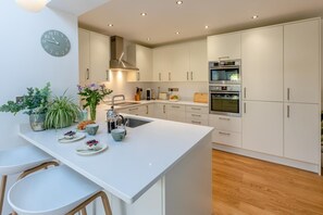 Una cocina moderna con armarios blancos, una isla central, horno empotrado y un reloj en la pared.