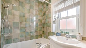 Une salle de bain équipée d’une baignoire, d’une douche, d’un lavabo et d’une fenêtre avec des stores.
