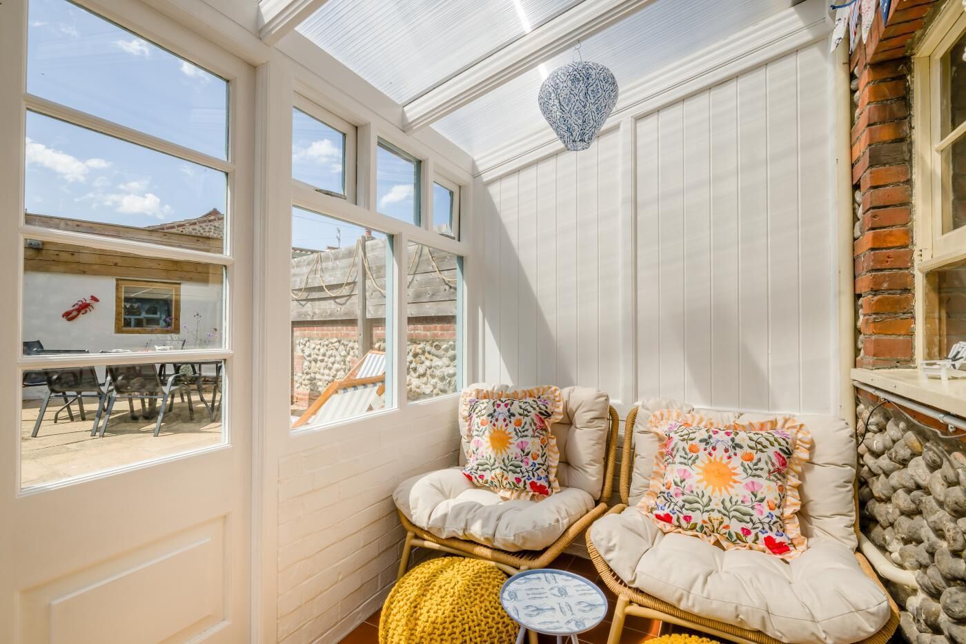 A sunlit room with a glass ceiling, wicker furniture, and a view of an outdoor patio.