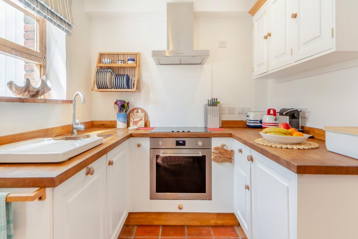 A compact kitchen with white cabinets, a stainless steel range hood, a built-in oven, and a wooden countertop.