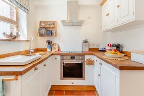 Une cuisine compacte avec des meubles blancs, une hotte en acier inoxydable, un four encastré et un plan de travail en bois.