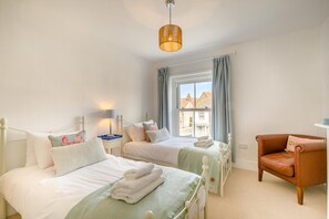 A bedroom with two beds, a window with curtains, a chair, and a hanging light fixture. - 4 Bed in Sheringham (oc-s30767) (Sheringham)