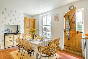 A dining area with a table set for four, surrounded by wicker chairs, a wooden cabinet, and a window with a view of the outside. - 4 Bed in Sheringham (oc-s30767) (Sheringham)