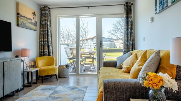 Ein modernes Wohnzimmer mit einer Couch, einem gelben Sessel, einem Flachbildfernseher und einem Essbereich mit Gartenmöbeln.