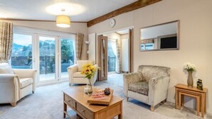 A spacious living room with a large window, a sofa, a chair, a coffee table with a vase of flowers, and a television mounted on the wall. - 2 Bed in St. Fillans (oc-l30650) (Saint Fillans)