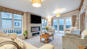 A spacious living room with a fireplace, comfortable seating, a flat-screen TV, and large windows offering a view of the outside. - 2 Bed in St. Fillans (oc-l30650) (Saint Fillans)