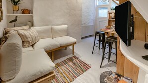 Een moderne woonkamer met een bank, een eethoek met tafel en stoelen, een televisie en een trap.