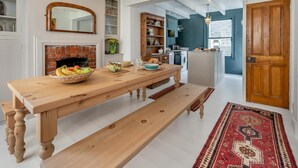 Un'area pranzo con un tavolo in legno, panche, una ciotola di frutta e un camino.