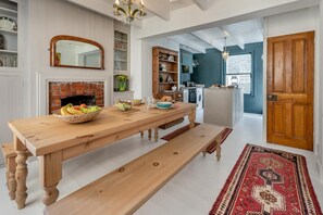 Un coin repas avec une table en bois, des bancs, un panier de fruits et une cheminée.