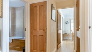 Een hal met een houten deur, een badkamer met douche, en een eethoek met tafel en stoelen.