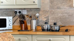 Een keuken met een magnetron, messen, lepels en pannen op het aanrecht.