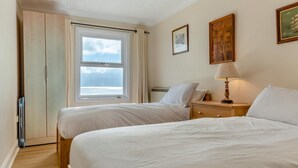 Een slaapkamer met twee bedden, een raam met gordijnen, een nachtkastje met een lamp en een lijst met een afbeelding aan de muur.
