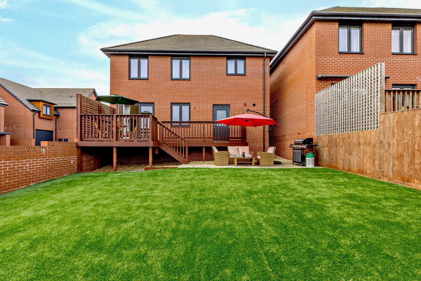 A residential backyard with a grassy lawn, a wooden deck, and a barbecue grill.