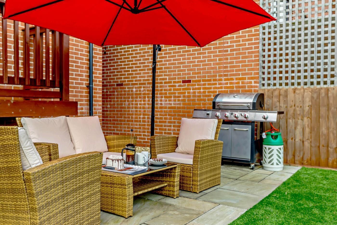 A patio with wicker furniture, a grill, and a red umbrella.