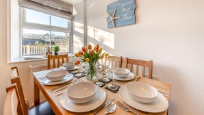 A dining area with a table set for four, a window with a view, and a wall sign reading "Welcome to our Beach House". - 3 Bed in Saundersfoot (oc-c30698) (Saundersfoot)