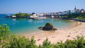A coastal town with a sandy beach, a rocky outcrop, and a mix of residential and commercial buildings. - 3 Bed in Saundersfoot (oc-c30698) (Saundersfoot)