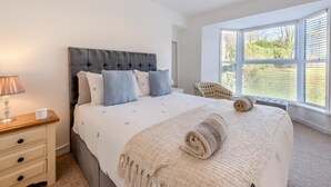 A bedroom with a large bed, a bedside table, a lamp, and a window with blinds. - 3 Bed in Saundersfoot (oc-c30698) (Saundersfoot)