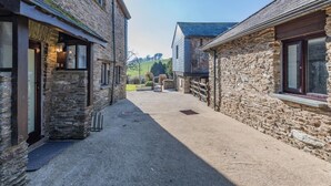 A narrow stone alleyway between two buildings with a gravel path, leading to a grassy area with trees and a hill in the distance. - 4 Bed in East Allington (oc-k30711) (East Allington)
