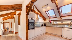 A modern kitchen with wooden beams, a built-in oven, and a large window. - 4 Bed in East Allington (oc-k30711) (East Allington)