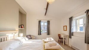 Une chambre d’hôtel avec deux lits, un bureau et une chaise. Il y a des serviettes sur le lit et une fenêtre avec des rideaux.