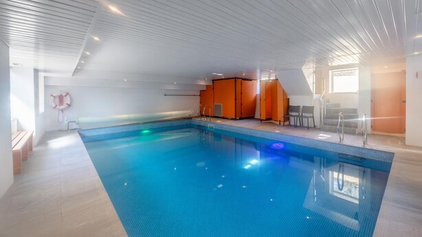 Une piscine intérieure avec un sol carrelé, une bouée de sauvetage fixée au mur et des barrières de sécurité orange.