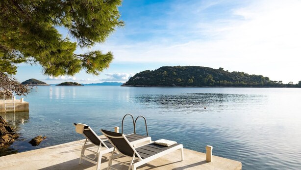 A serene lakeside setting with a concrete dock, two lounge chairs, and a clear view of a distant island. - Nice home in Karbuni with WiFi (Karbuni)