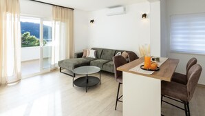 A modern living room with a sofa, coffee table, and dining area. There is a view of the outdoors through large windows. - Nice home in Karbuni with WiFi (Karbuni)