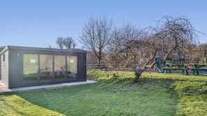 A modern building with large glass windows and a flat roof, surrounded by a grassy area and trees. - 3 Bed in East Allington (oc-m30710) (East Allington)