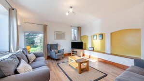 A modern living room with a grey sofa, a blue armchair, a wooden coffee table, and a flat-screen TV. - 3 Bed in East Allington (oc-m30710) (East Allington)