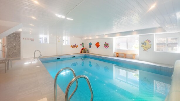 En indendørs swimmingpool med krystalklart vand, en metalstige og farverige dekorationer på væggene.