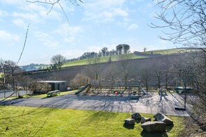 A playground with a slide, climbing structure, and a small building, surrounded by grass and trees. - 4 Bed in East Allington (oc-k30713) (East Allington)