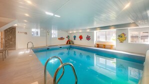 Une piscine intérieure offrant une vue dégagée sur l’espace piscine, un banc en bois et des décorations murales colorées.