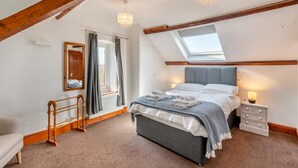 Une chambre avec un plafond en pente, un lit avec des serviettes soigneusement pliées, une table de chevet avec une lampe et une fenêtre avec des rideaux.