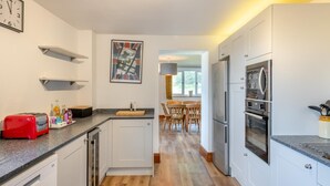 Une cuisine moderne avec des meubles blancs, un grille-pain rouge et un coin repas doté de chaises en bois.