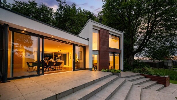 Een modern huis met een glazen ingang, een eethoek met stoelen, en een trap die naar de entree leidt.