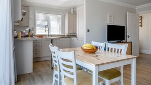 Une cuisine de taille réduite avec des meubles blancs, une table à manger avec des chaises et un téléviseur posé sur un meuble.
