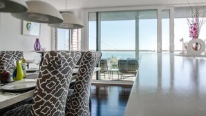 Un comedor moderno con sillas estampadas, una mesa con cubierta de vidrio e iluminación colgante.