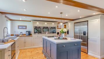 A modern kitchen with a central island, built-in ovens, a refrigerator, and wooden flooring.
