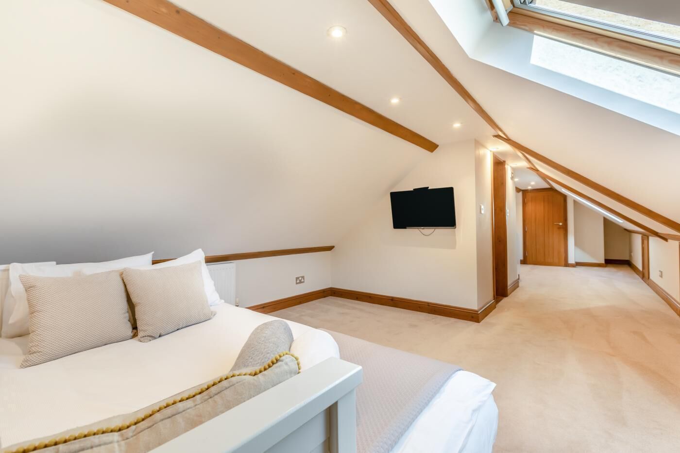 A bedroom with a sloped ceiling, a bed, a mounted TV, and a hallway leading to another room.