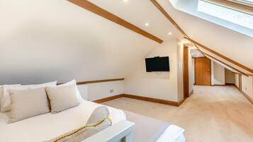 A bedroom with a sloped ceiling, a bed, a mounted TV, and a hallway leading to another room.