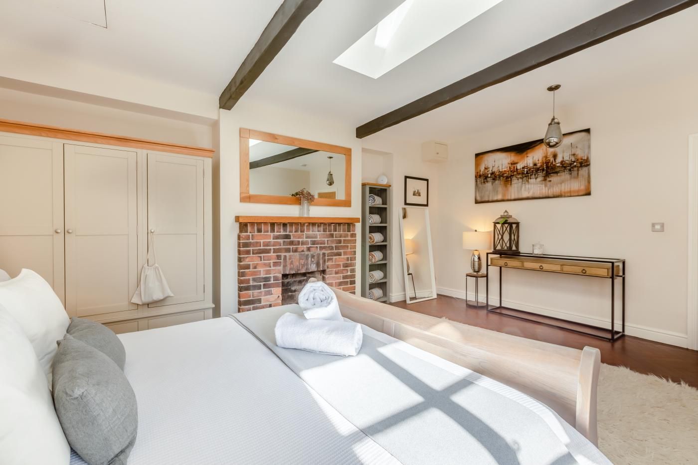 A bedroom with a bed, a fireplace, a console table, and a painting on the wall.