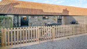 A stone building with a tiled roof, a wooden fence, and a patio with outdoor furniture. - 2 Bed in Clevedon (oc-t30786) (Clavedon)