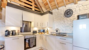 A modern kitchen with white cabinets, a stainless steel range hood, a built-in oven, a dishwasher, and a sink with a stone backsplash. - 2 Bed in Clevedon (oc-t30786) (Clavedon)